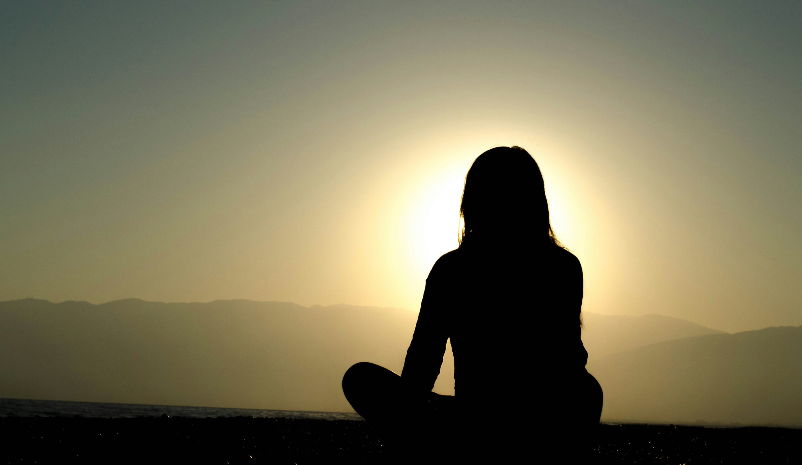 Woman sitting cross legged on the ground as a silhouette in front of the sun