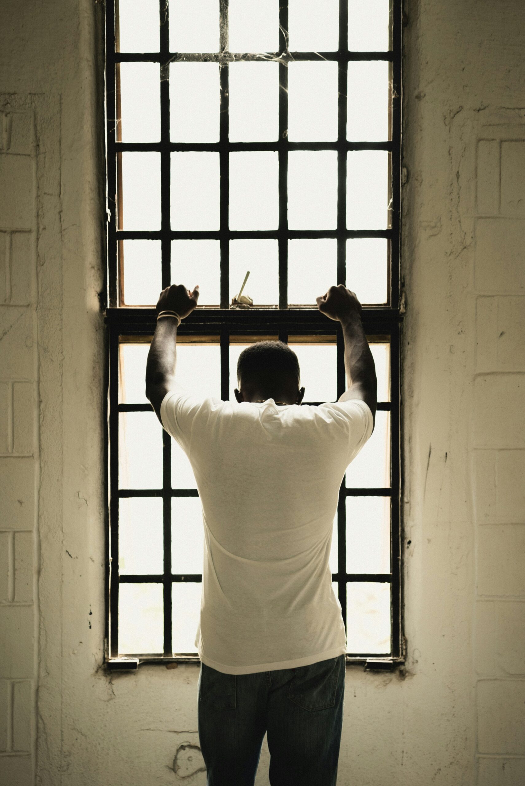 Man with his back to the camera, and his hands on the bars at a window